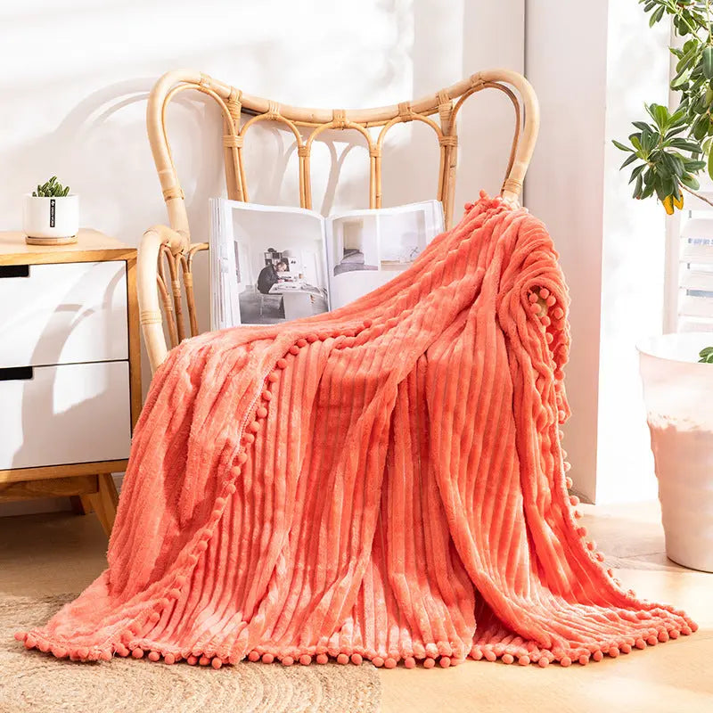 Velvet throw with pom edges draped over reading chair for minimalist home decor