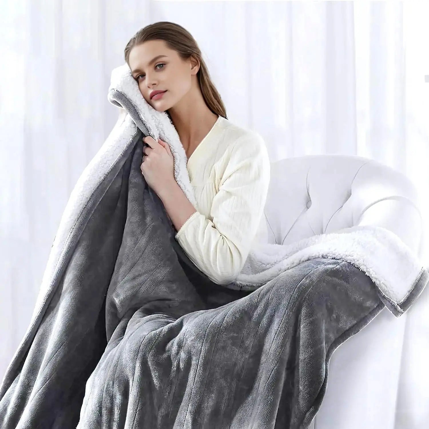 Woman in a white robe holding a gray blanket with white sherpa lining.