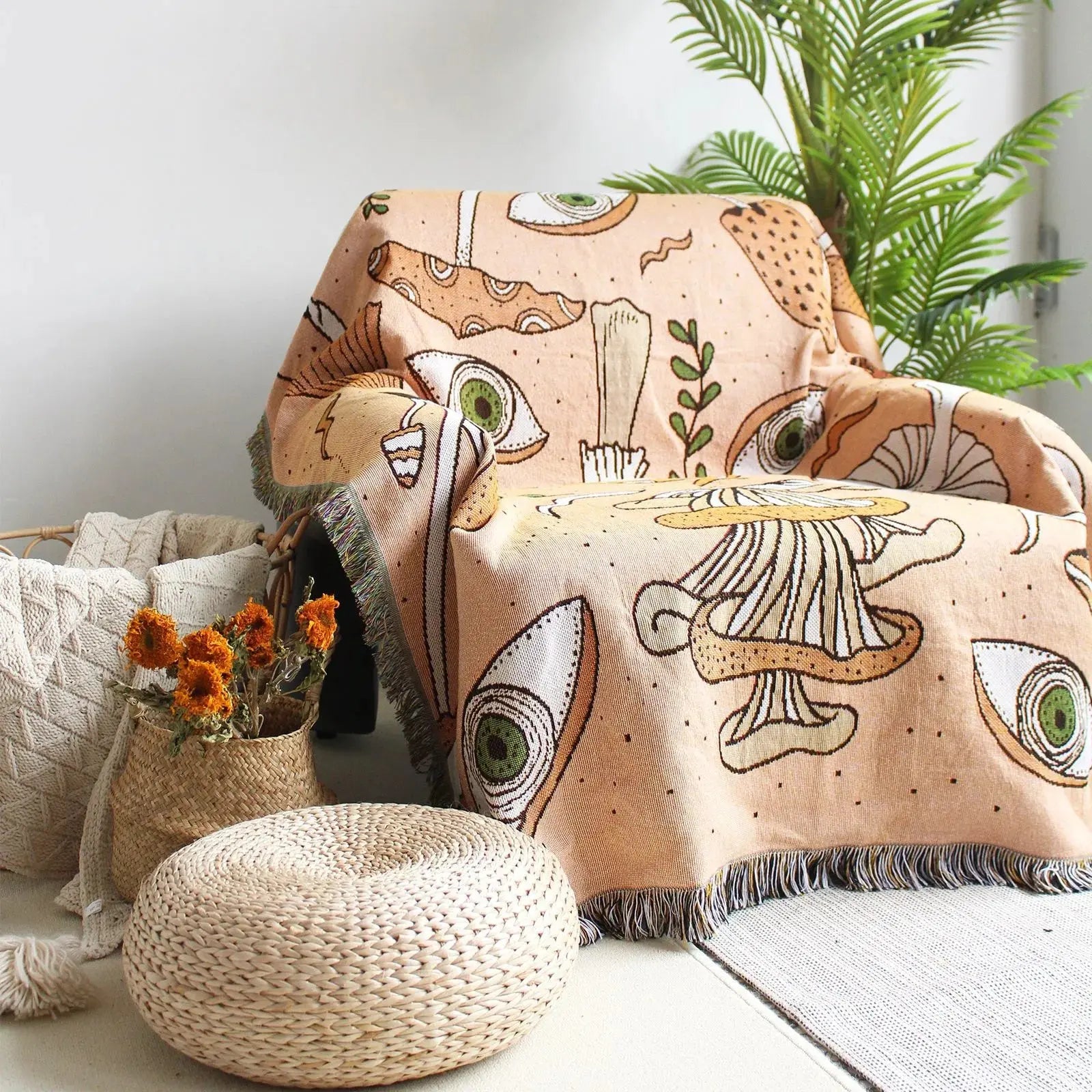 Decorative blanket with nature-themed design on a chair in a room with plants and a woven ottoman.