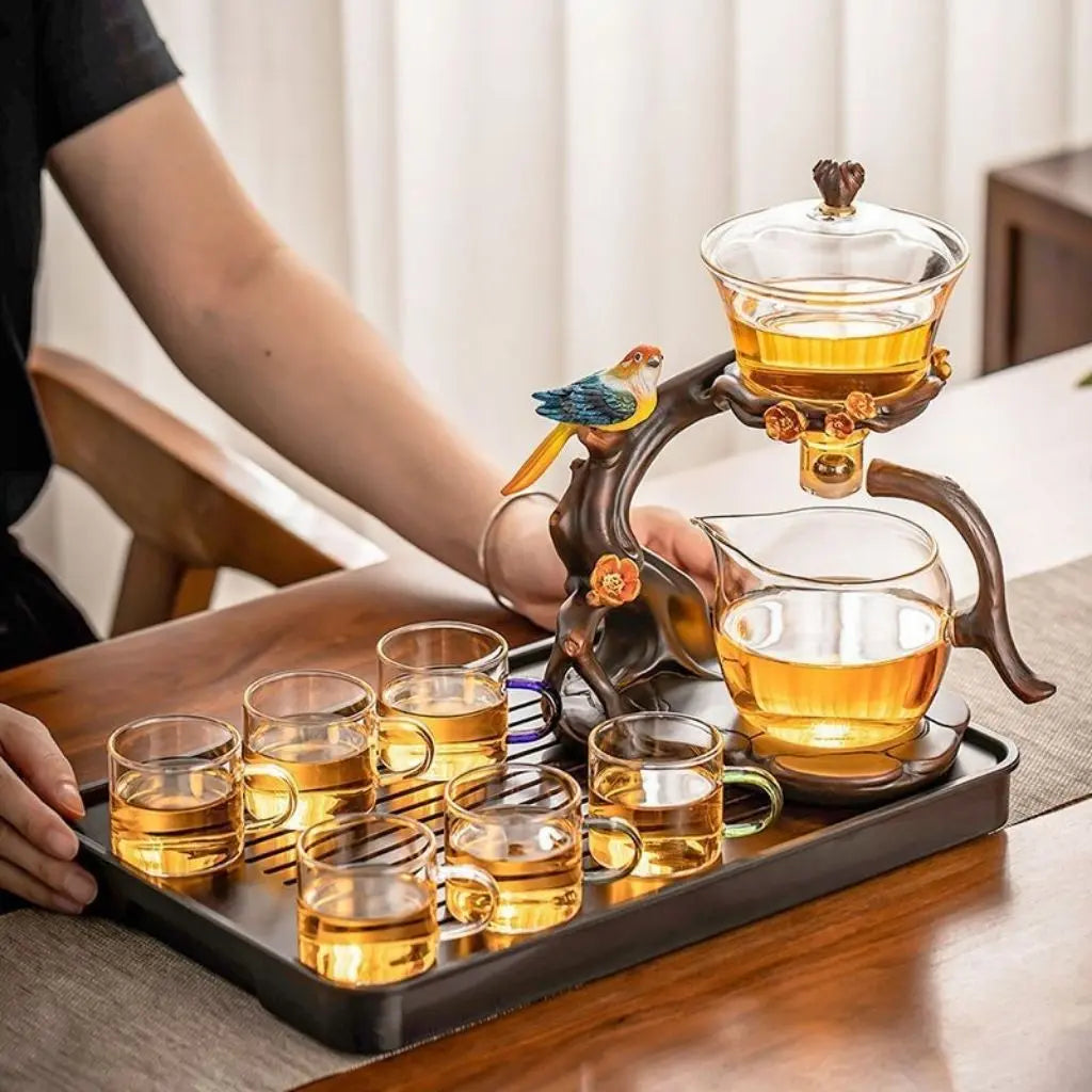 Tea set with glass cups and a teapot on a tray, with a person's hand holding the teapot.