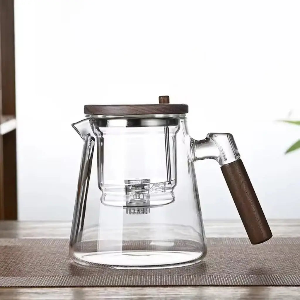 Clear glass coffee maker with wooden handle and lid on a light surface.