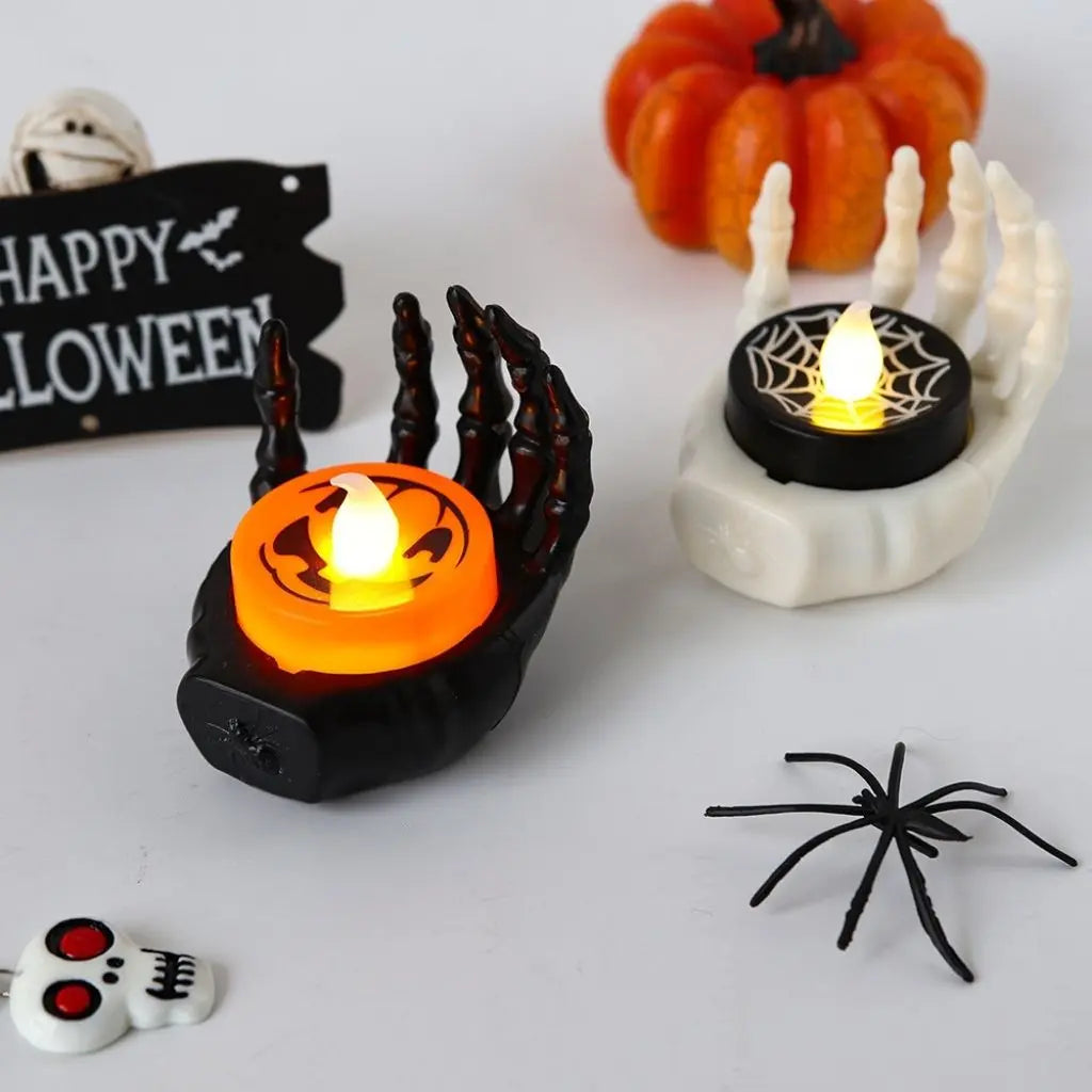 Halloween-themed decorative items including an LED black hand candle lamp holding a pumpkin, a white bone with a spider web, and a small skeleton skull on a white background.