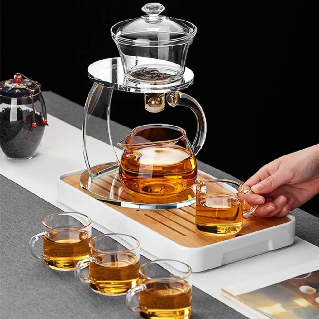Glass teapot and cups on a wooden tray with a hand pouring tea.