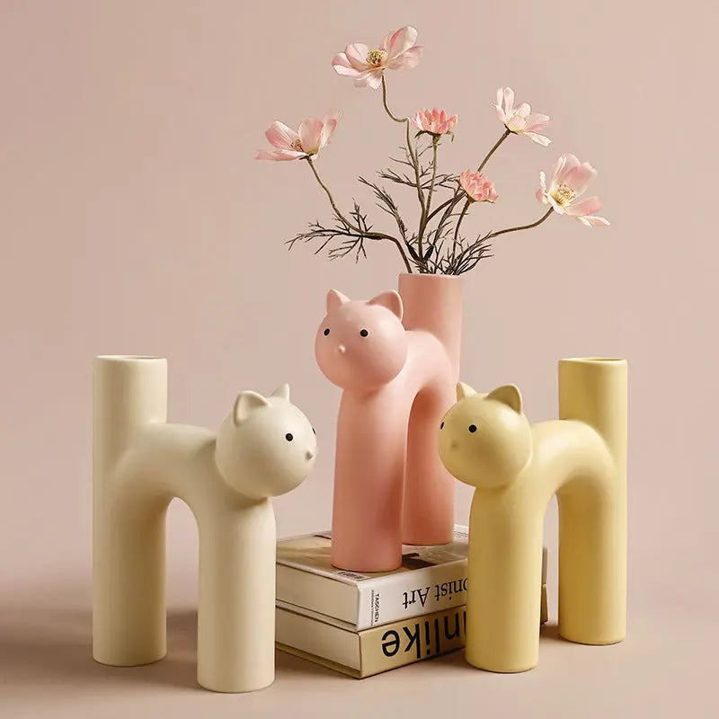 A set of porcelain vases with a cat-inspired design, in beige, pink, and white colors, displayed with flowers in one of them.
