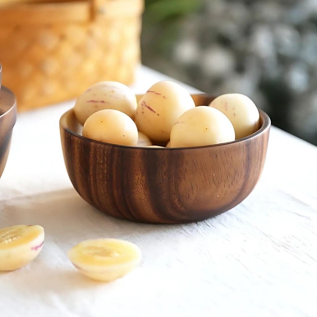 Wooden bowl filled with peeled potatoes on a light surface