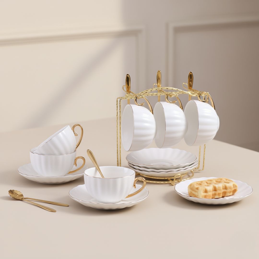 Gold rimmed ceramic tea cups with saucers and spoons arranged on decorative metal holder rack