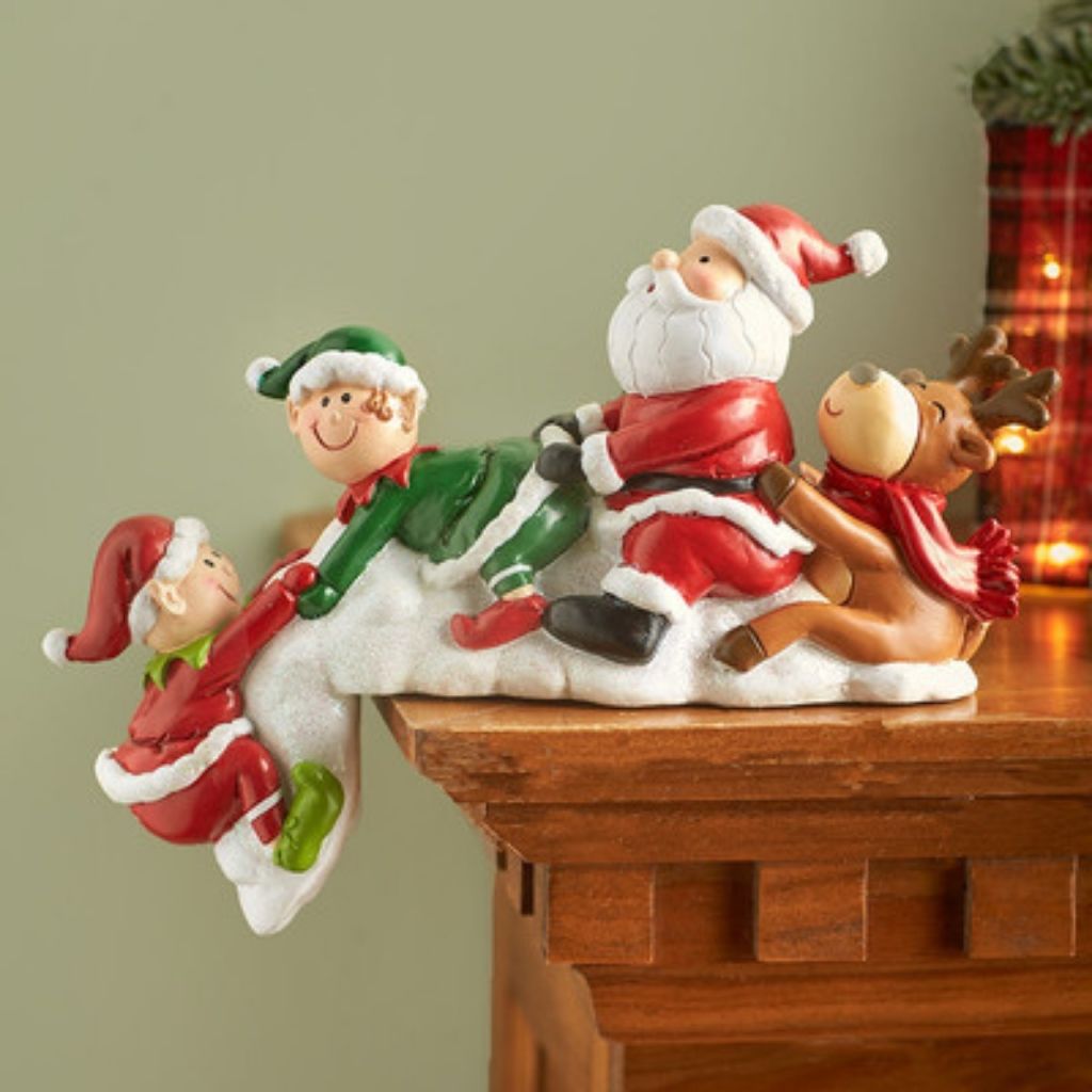 Decorative figurine of Santa, elf, and reindeer on a wooden surface with a neutral background.