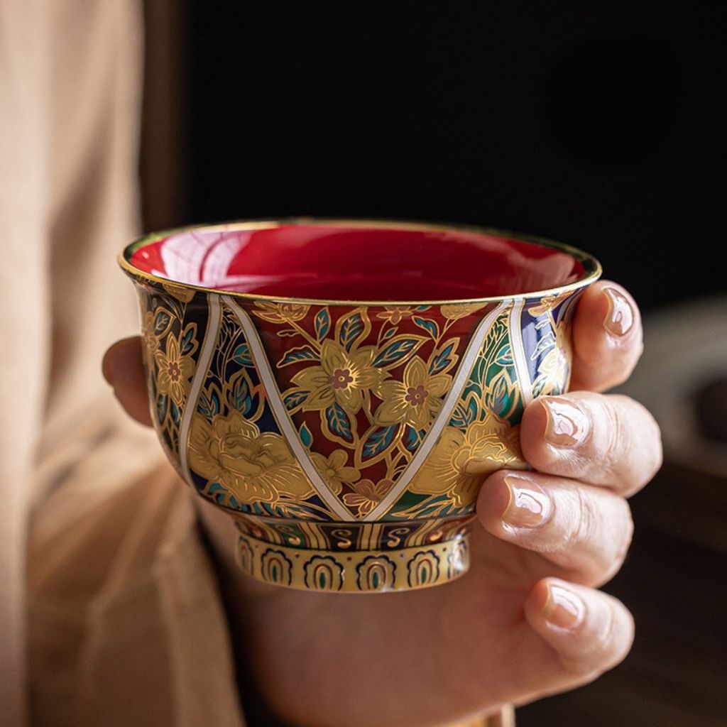 Hand holding a intricately designed cup with gold floral patterns