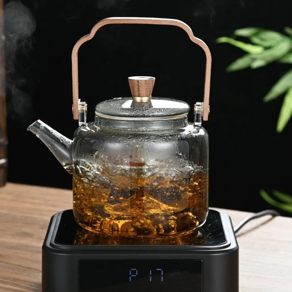 Glass teapot with a wooden handle on a black electric base, filled with tea.