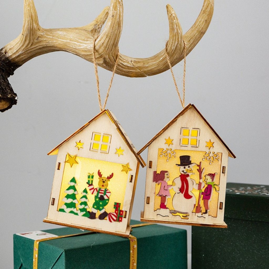 Two wooden house-shaped Christmas ornaments with festive designs hanging from antlers.