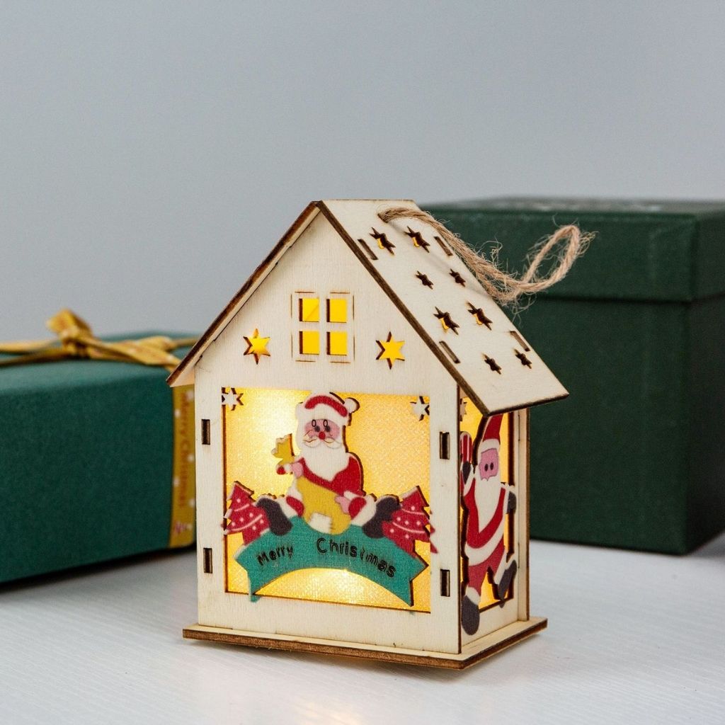 Decorative wooden house-shaped lantern with Santa Claus design, glowing inside, on a light background.
