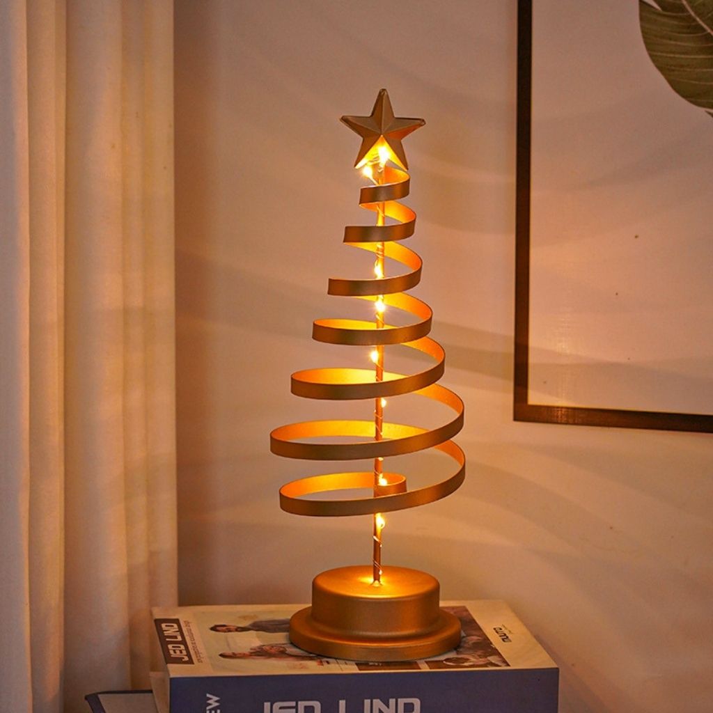 Decorative gold spiral Christmas tree lamp on a box against a neutral wall.