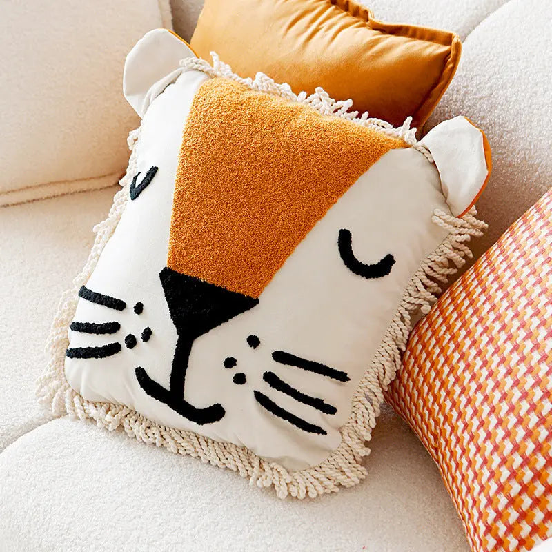 A decorative throw pillow with a lion face design, featuring a beige mane, black face details, and orange ears, displayed on a white chair.
