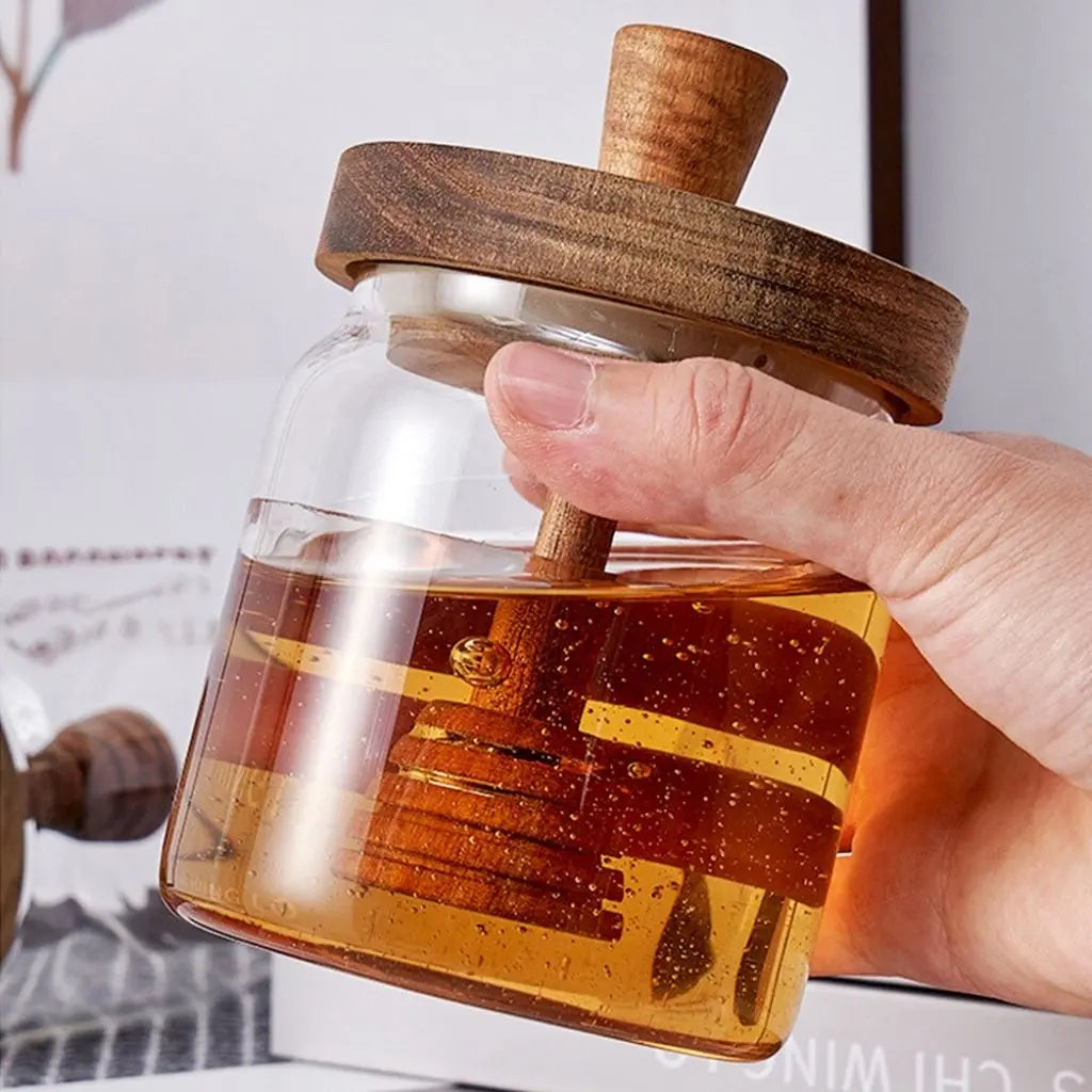 A glass honey jar with a wooden lid filled with honey.
