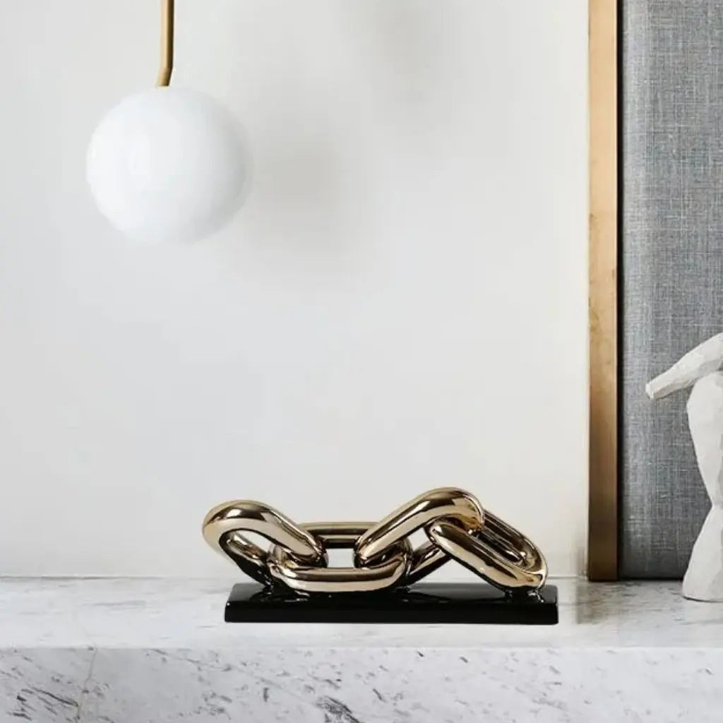 Gold chain-like sculpture on a black base in a modern interior setting.
