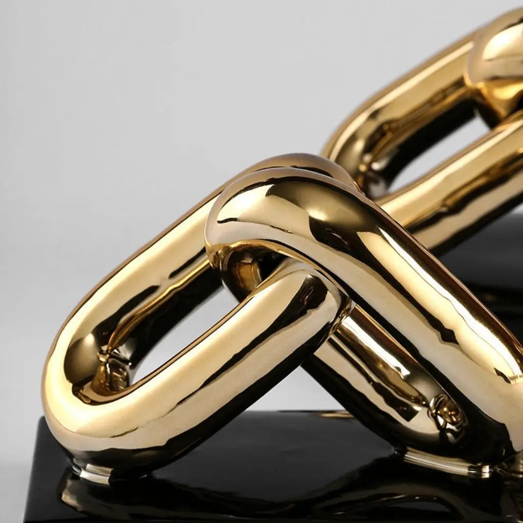 Close-up of two interlocking gold chains on a reflective surface with a gray background