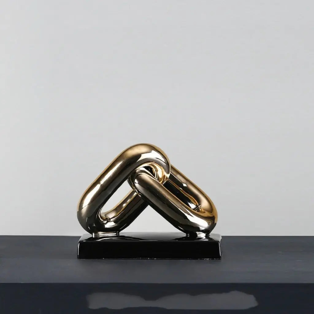 Gold chain link sculpture on a black base against a gray background
