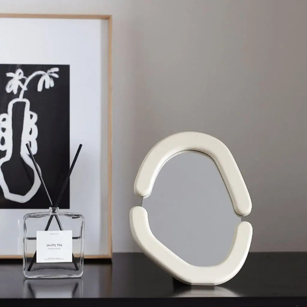 Decorative white abstract sculpture on a dark surface with a framed black and white artwork in the background.