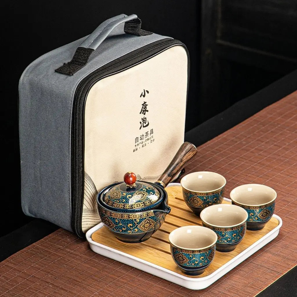 Tea set with four cups and a pot on a tray next to a gray carrying case.
