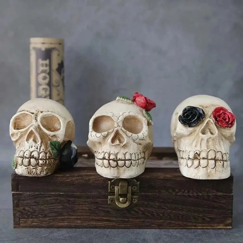Three decorative skulls with floral arrangements on a wooden box against a gray background