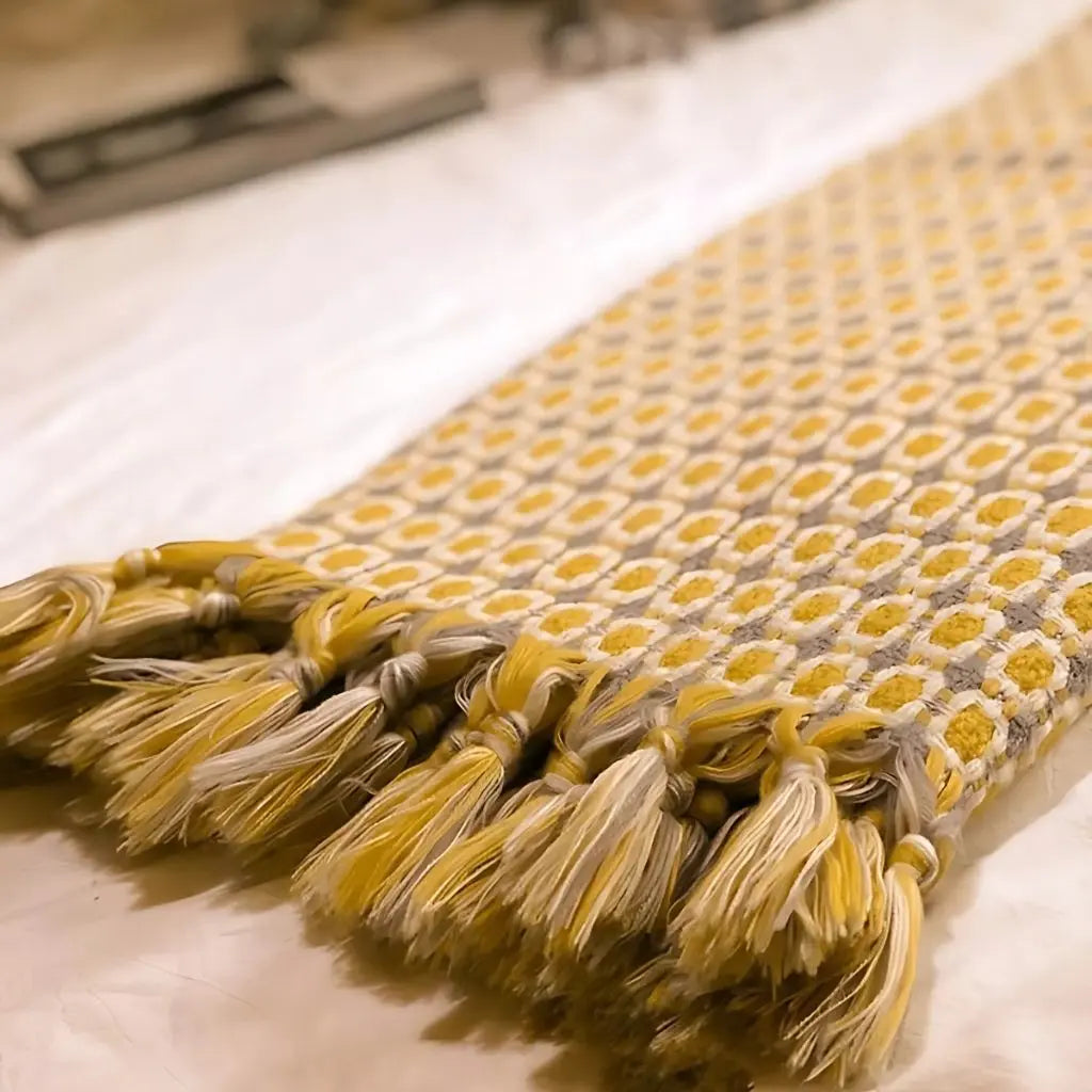Geometric throw blanket in warm yellow tone featuring Nordic knit construction and tassel trim