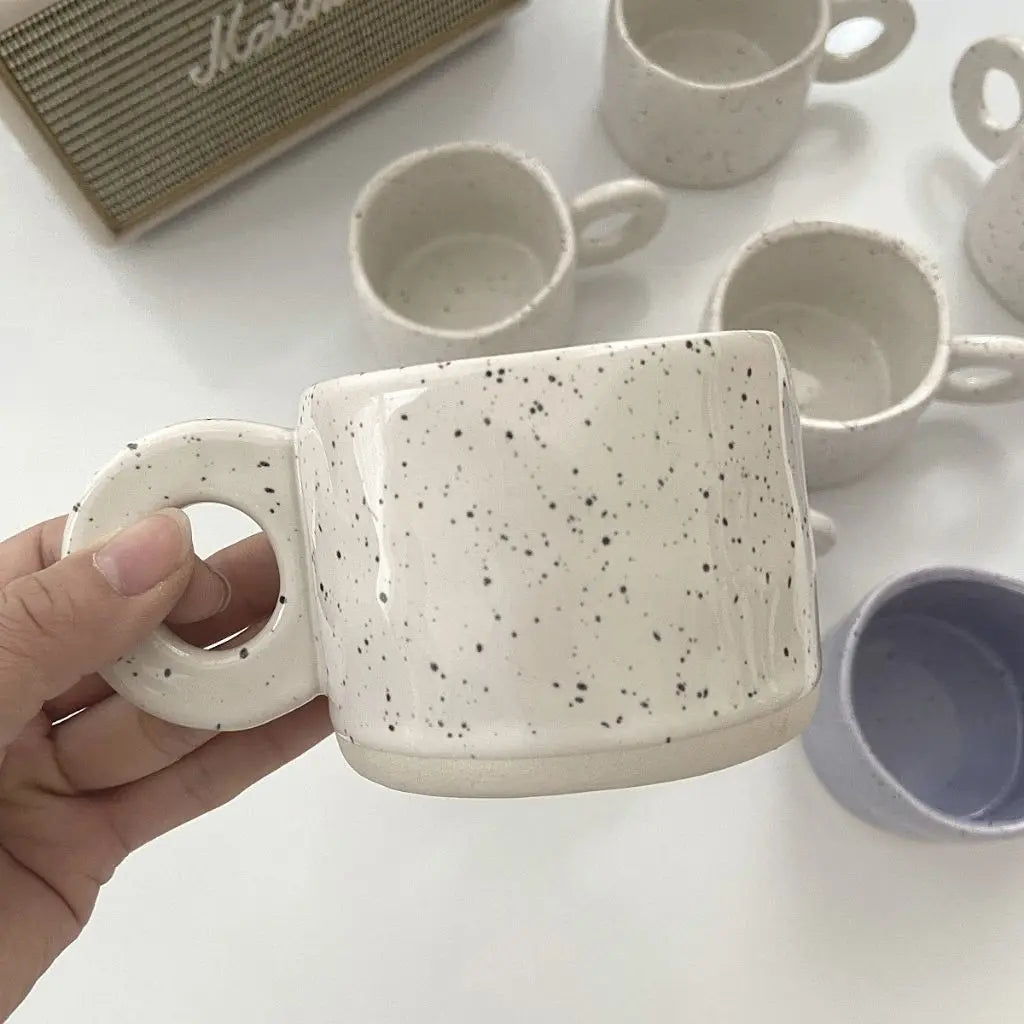 Speckled ceramic coffee mug with retro glaze pattern and modern circular handle construction.