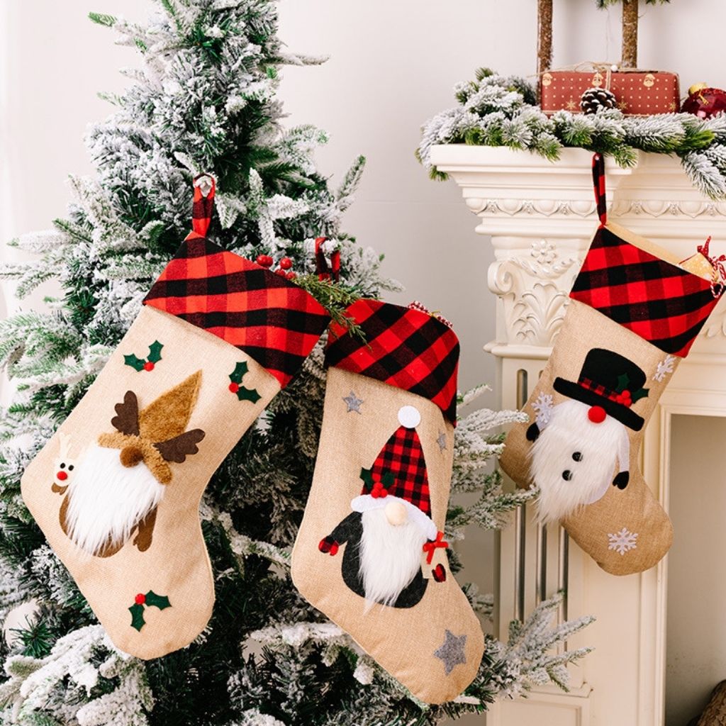 Three Christmas stockings with festive designs hanging on a tree.