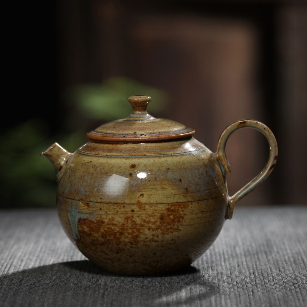 Angled view of handmade pottery teapot with curved handle and earth tone glaze