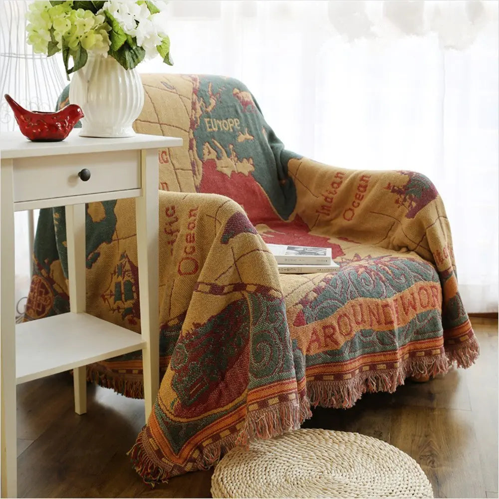Decorative blanket with world map design draped over a chair in a room with a small table and flowers.