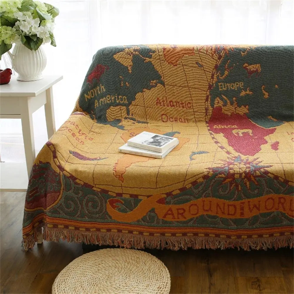 World map-themed blanket draped over a sofa with a small stool and flowers in the background.