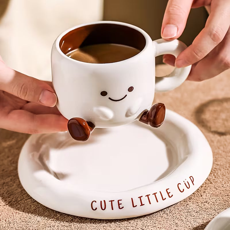 Cute white cup with smiling face design on a matching saucer, held by hands.