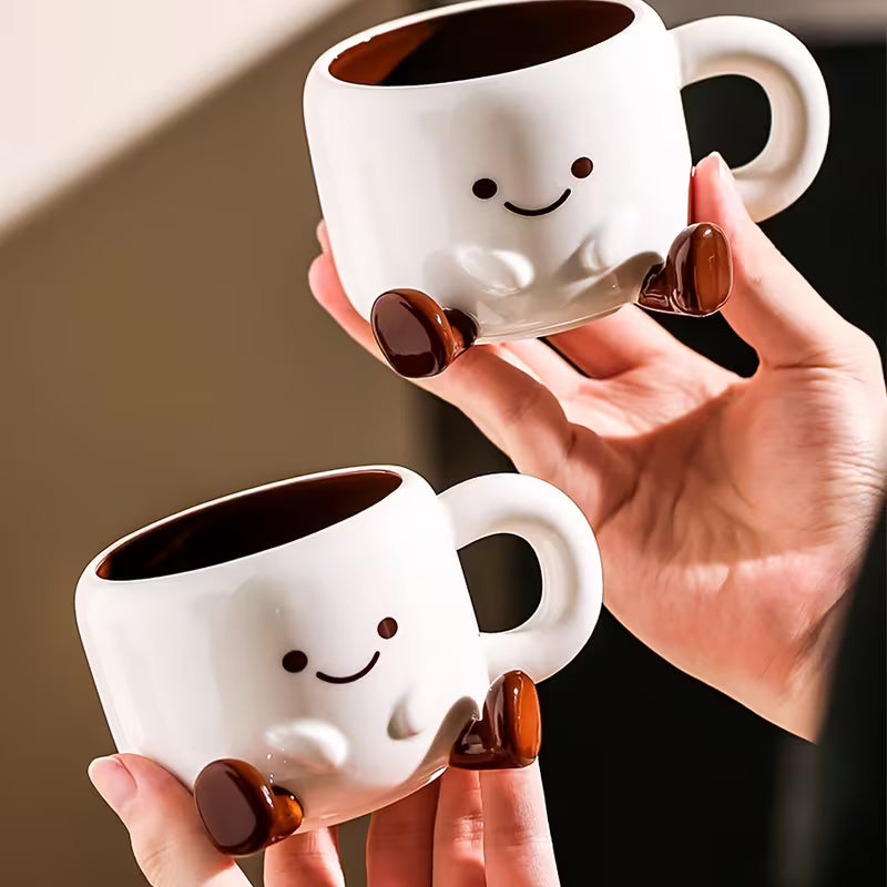 Two white mugs with smiley faces held by a hand against a neutral background