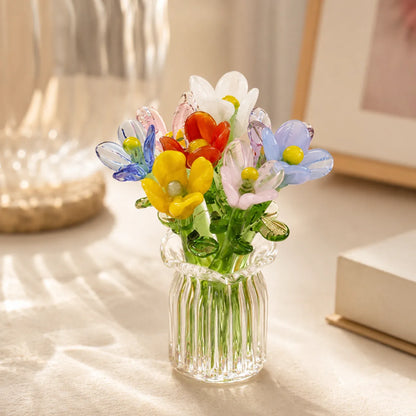 Clear glass vase with colorful artificial flowers on a light surface