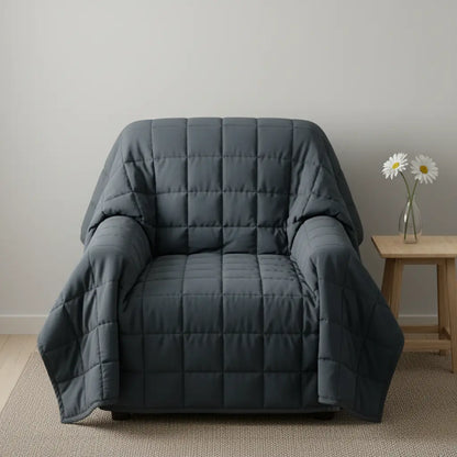 Gray quilted armchair cover draped over a chair in a room with a small table and flowers.