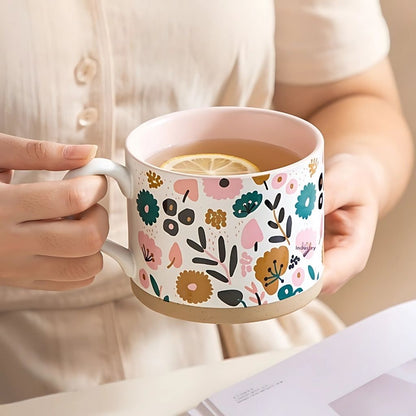 Person holding a floral-patterned mug with a drink, wearing a light-colored shirt.