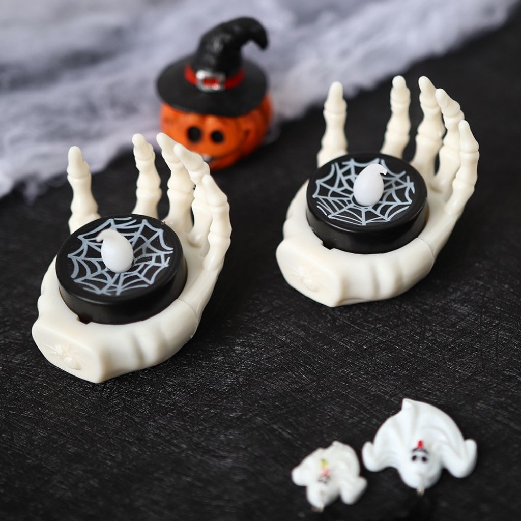 Halloween-themed candle LED lamp with skeleton hands and spider web design on a dark surface.