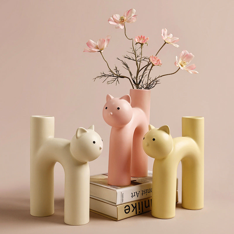 A set of porcelain vases with a cat-inspired design, in beige, pink, and white colors, displayed with flowers in one of them.