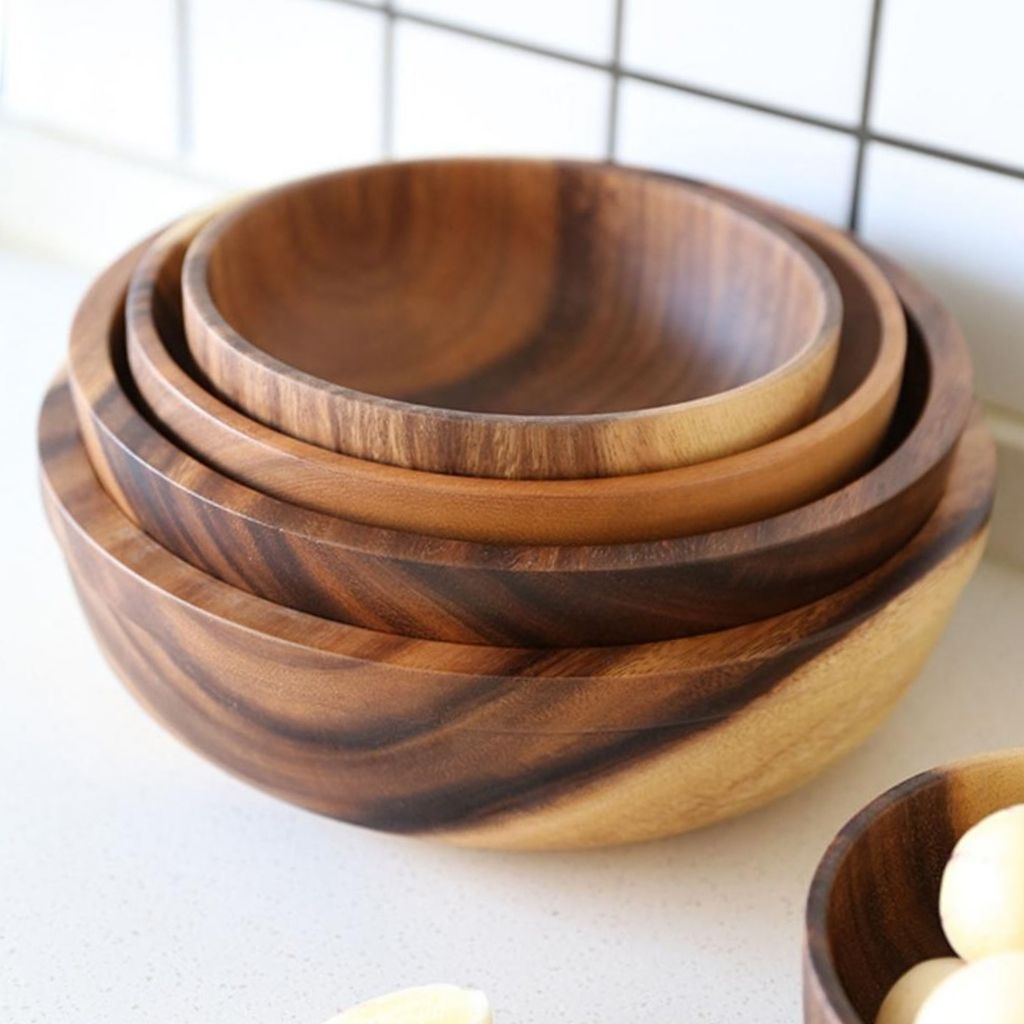Set of three wooden bowls stacked on a light surface with a grid-patterned background