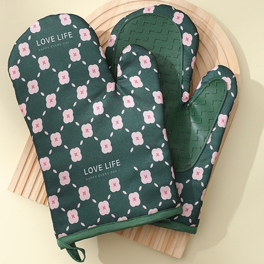 Green oven mitts with pink floral pattern and 'Love Life' text on a wooden board.