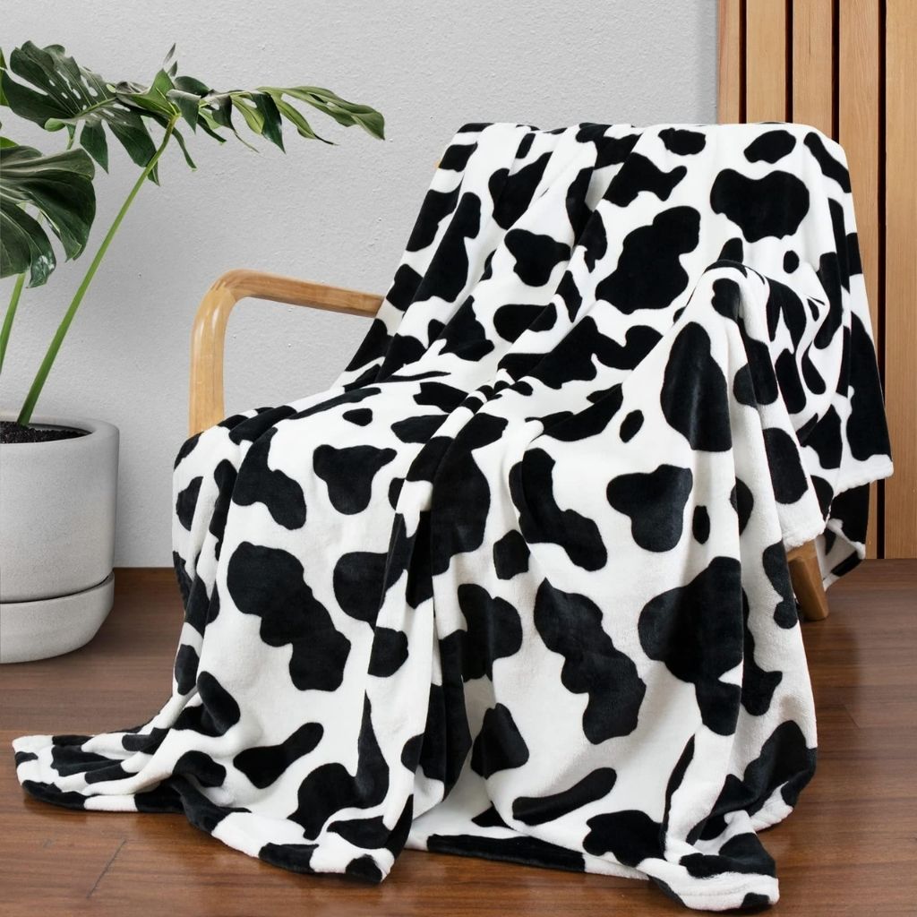  Ultra-soft flannel throw with classic cow print design draped over bed for cozy farmhouse bedroom decor