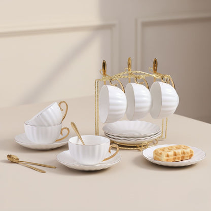 Gold rimmed ceramic tea cups with saucers and spoons arranged on decorative metal holder rack
