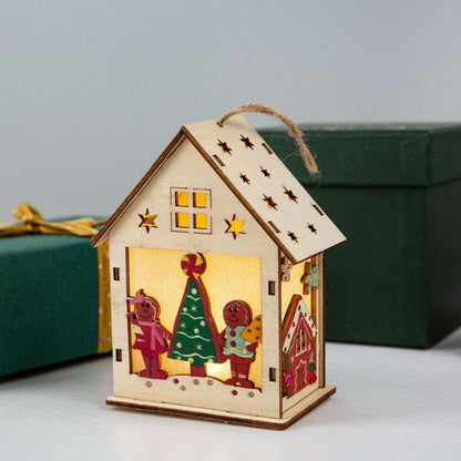 Wooden house-shaped lantern with Christmas design, hanging against a gray background with green gift boxes.