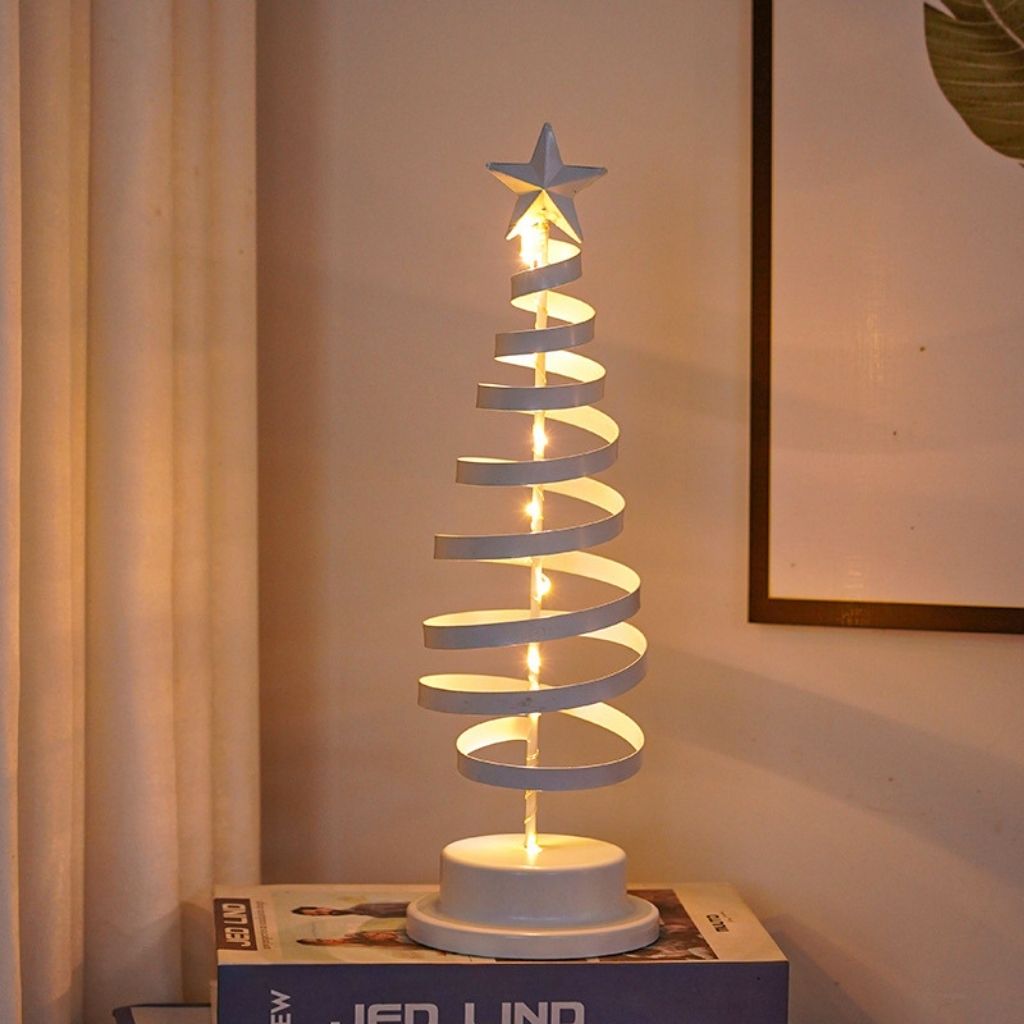 Decorative spiral Christmas tree lamp with a star on top, placed on a box against a neutral wall.
