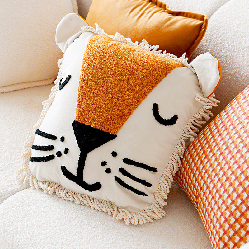 A decorative throw pillow with a lion face design, featuring a beige mane, black face details, and orange ears, displayed on a white chair.