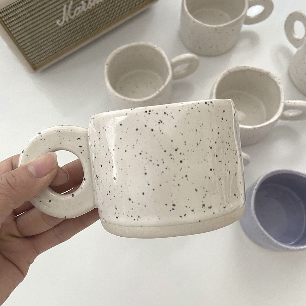 Speckled ceramic coffee mug with retro glaze pattern and modern circular handle construction.