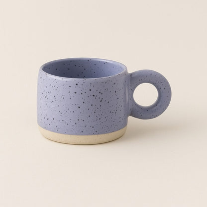 Ceramic coffee mug featuring distinctive circular handle and speckled texture for comfortable grip