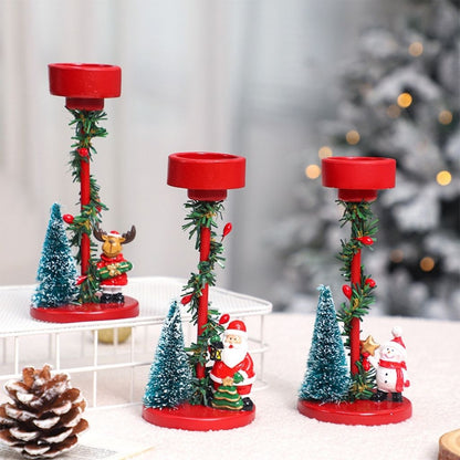 Resin candle stand with miniature Christmas scene and wrapped greenery on white base