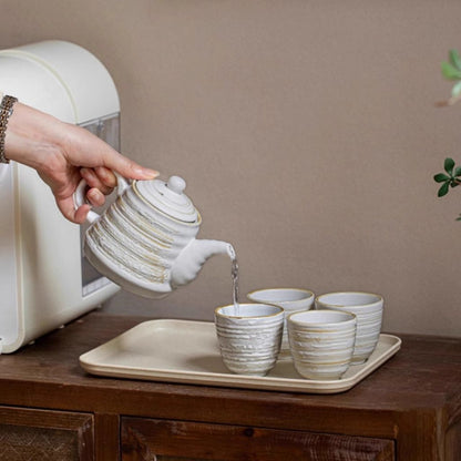 Ceramic tea set arranged on wooden tray for serving with teapot and four matching cups