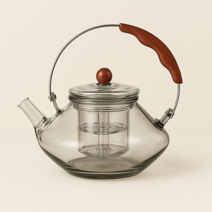 Clear glass teapot with a wooden handle and lid knob on a beige background