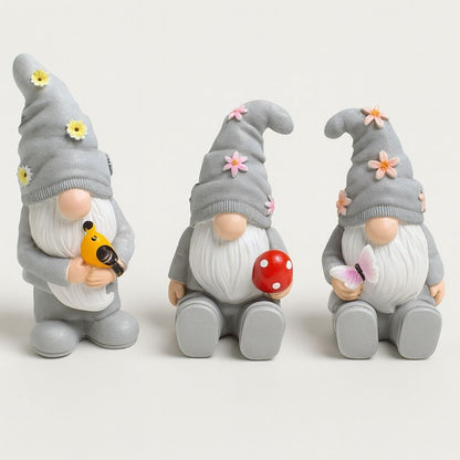 Three resin garden gnomes with colorful hats and beards displayed together on outdoor surface